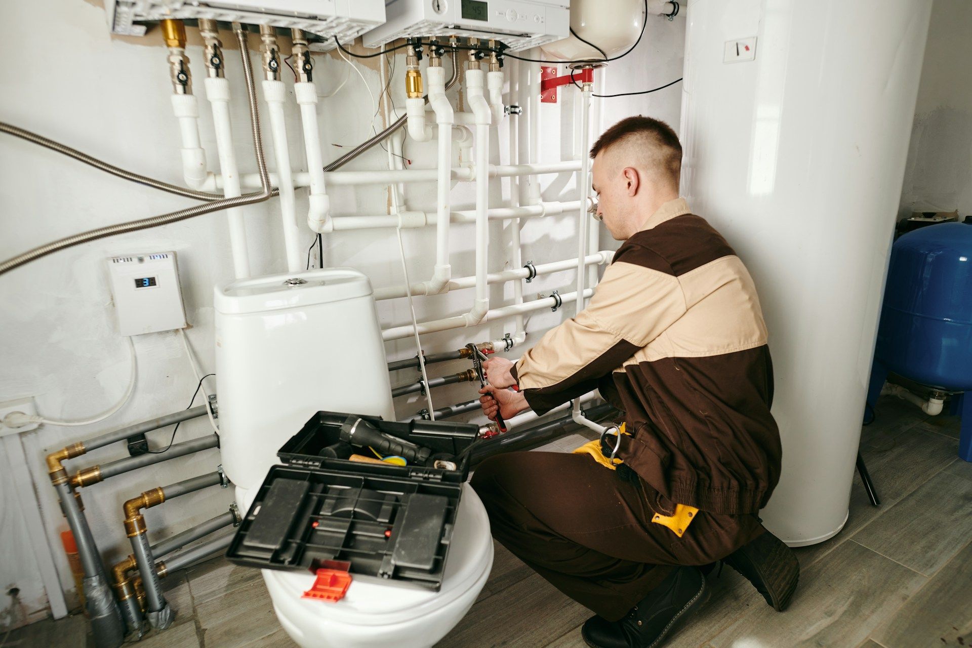 Technician repairing plumbing under a sink in a utility room, with tools spread out nearby