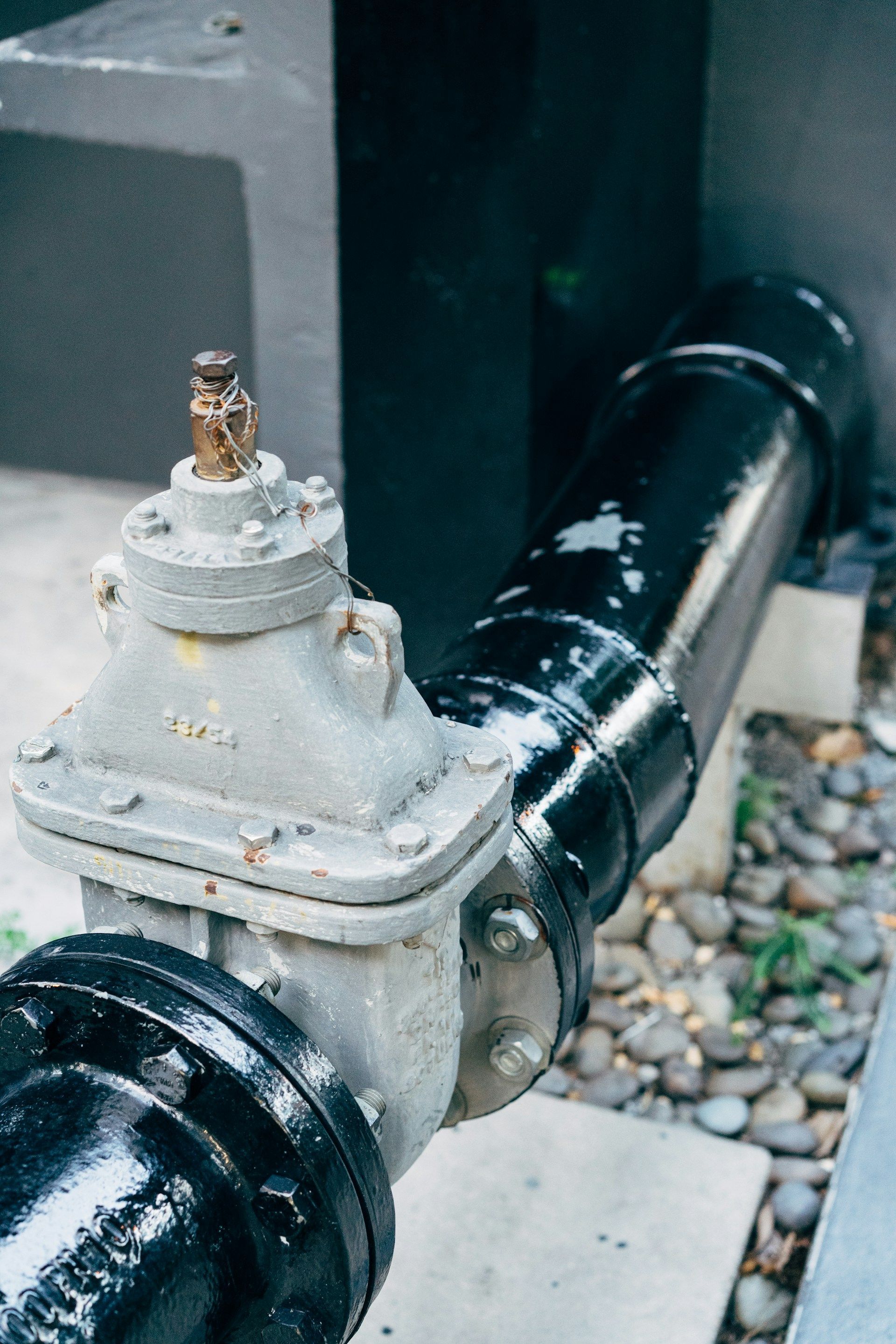 Close-up of a black gas pipe and gray shutoff valve beside a building wall