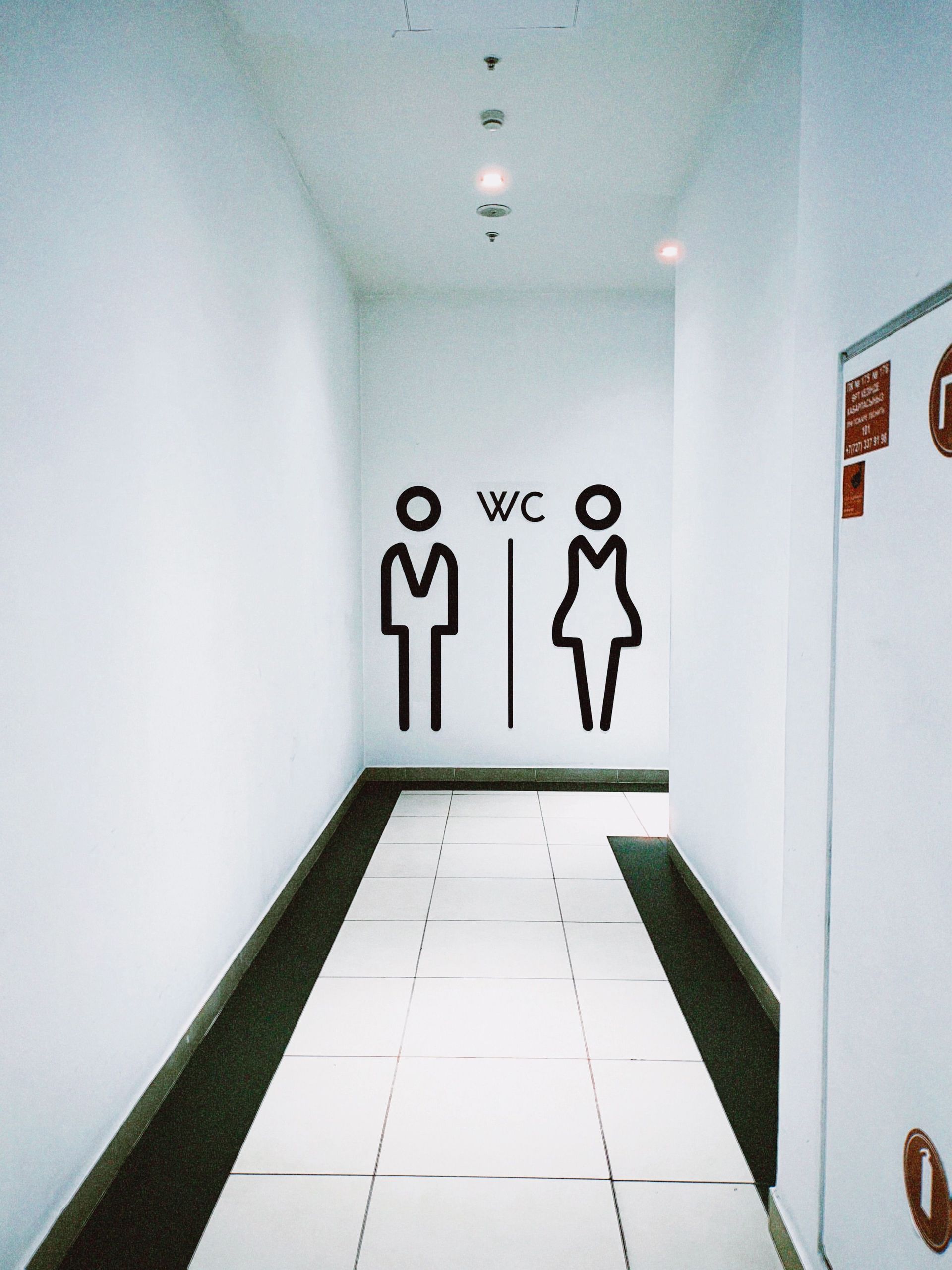 Narrow white hallway leading to WC restroom signs for men and women