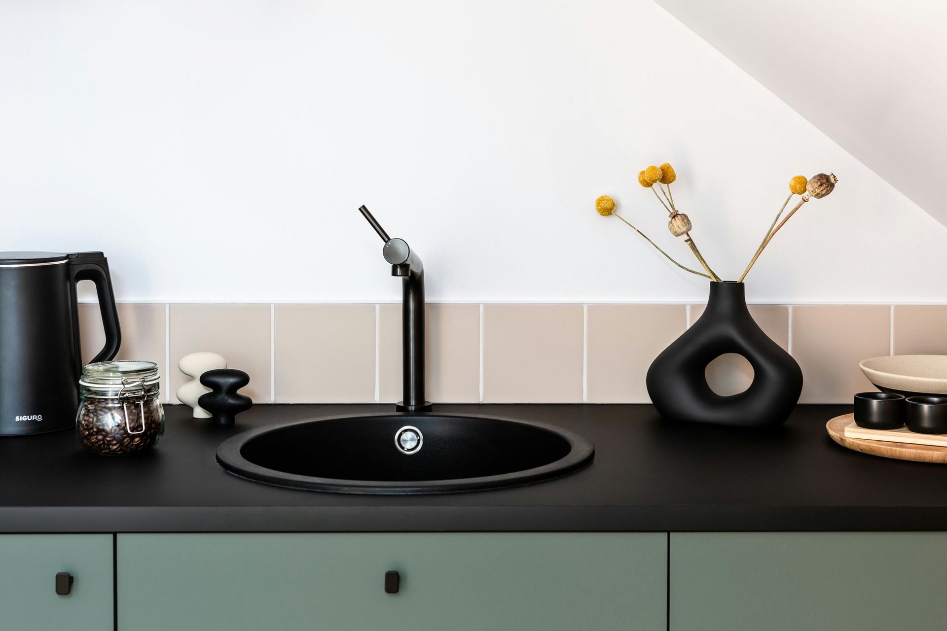 Modern minimalist kitchen counter with black sink, faucet, kettle, jars, and a black vase with yellow flowers