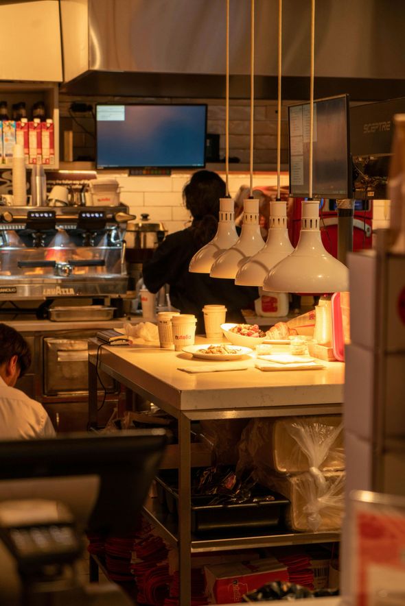 Busy café counter with hanging white lamps, pastries, and a worker behind the counter