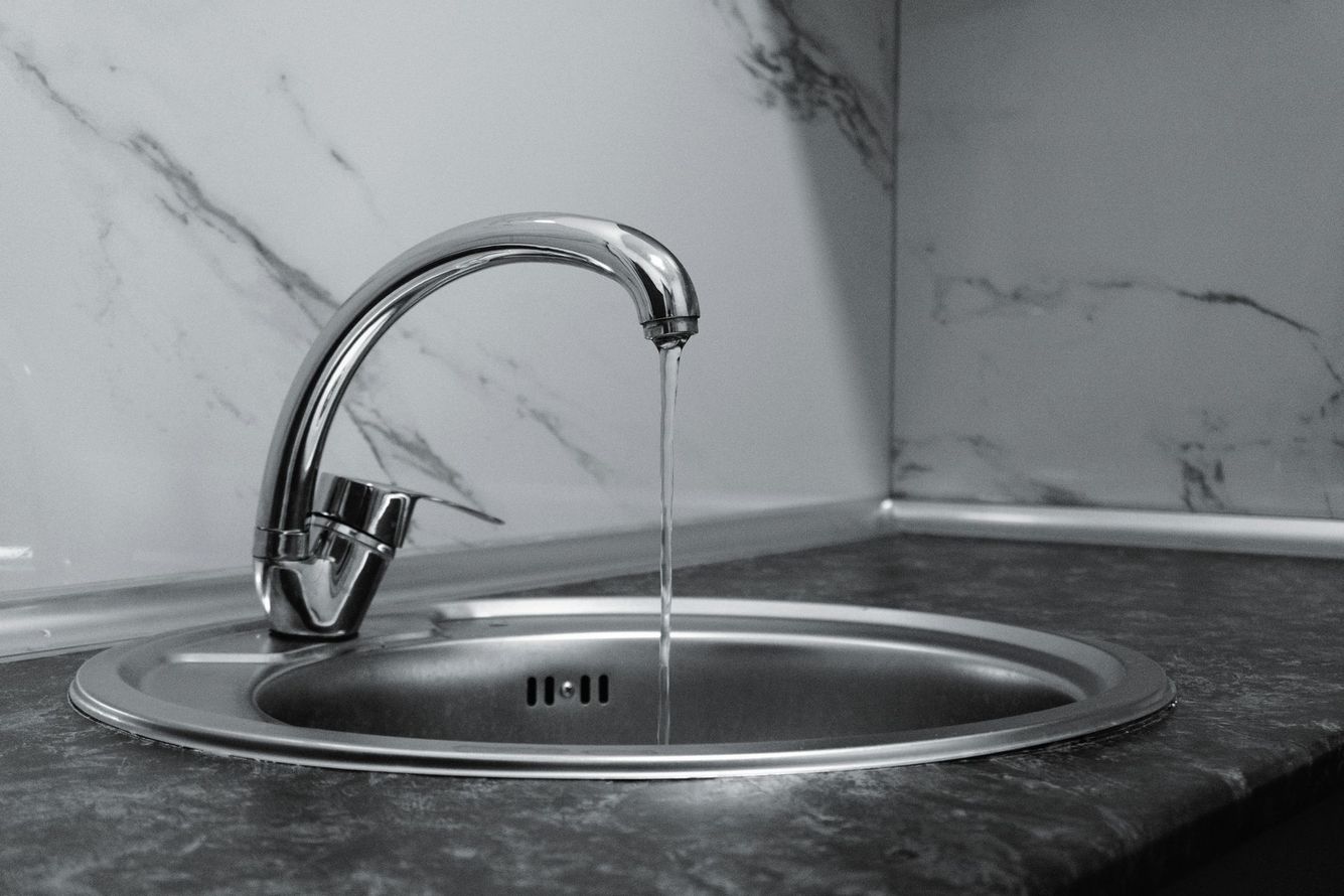 Chrome faucet running into a round kitchen sink on a marble countertop