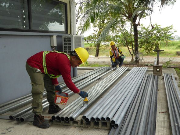 Worker in yellow hard hat loading metal pipes at a construction site