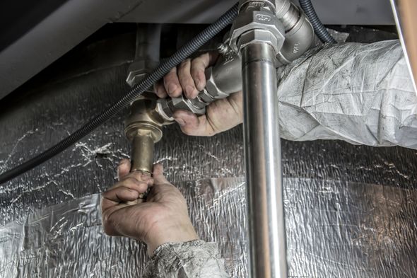 Hands installing a brass pipe fitting under a sink with a wrench, on a reflective silver insulated surface