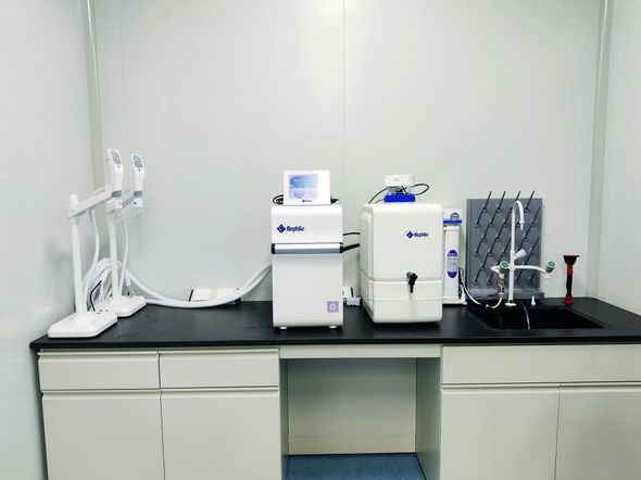 Laboratory benchtop with medical testing equipment and devices on a black counter against a white wall