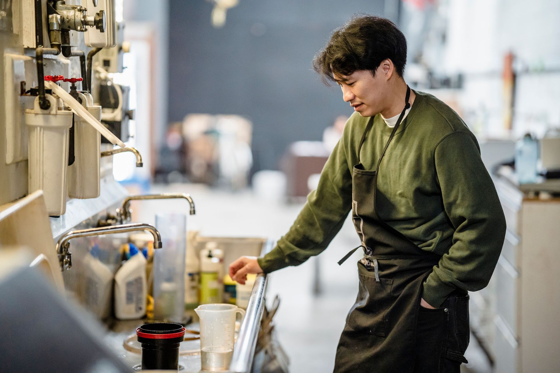Person in a green sweater working at a sink in an industrial kitchen or workshop