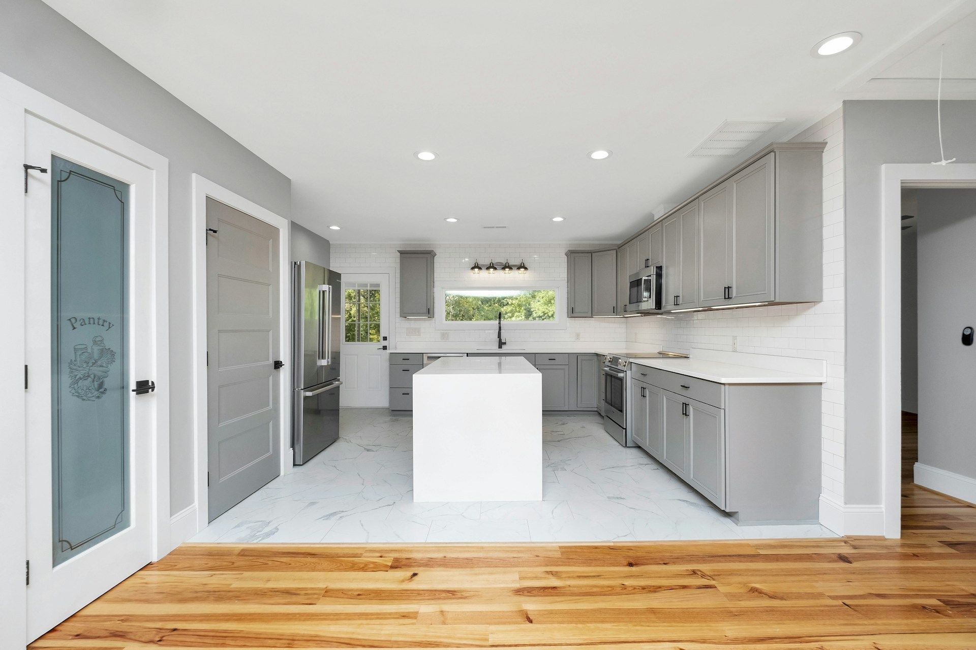 Bright modern kitchen with white and gray cabinets, island, large windows, and hardwood floor