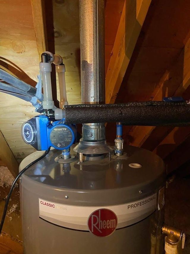 A water heater is sitting in the attic next to a pipe.