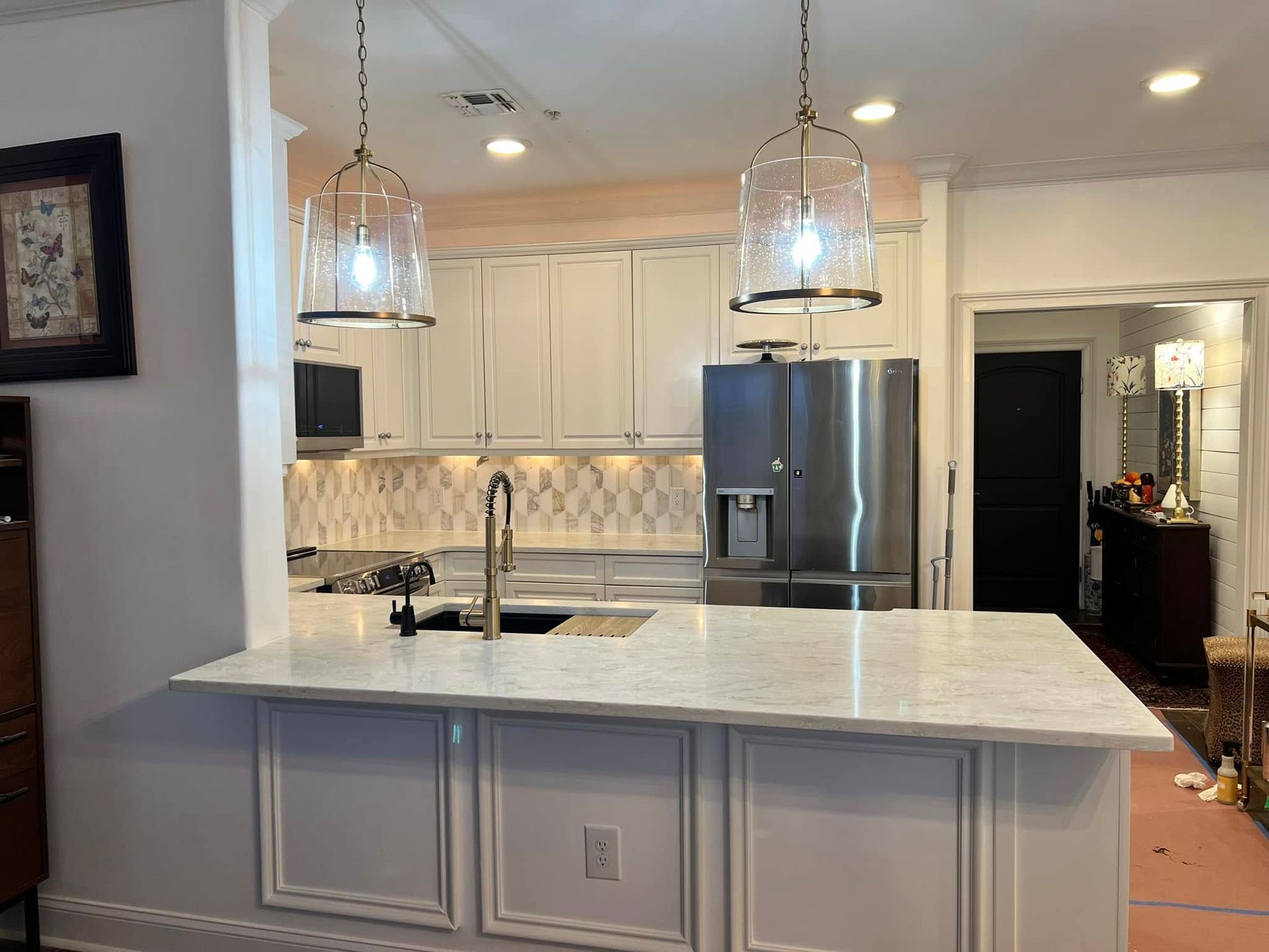A kitchen with white cabinets , a stainless steel refrigerator, a sink, and a large island.