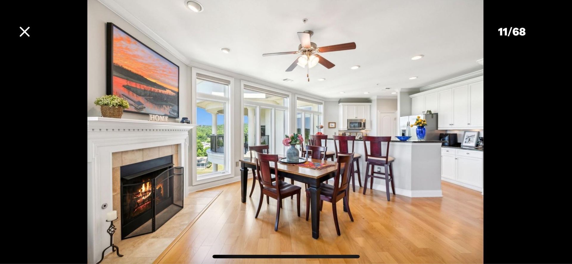A living room with a fireplace, dining table, chairs and a ceiling fan