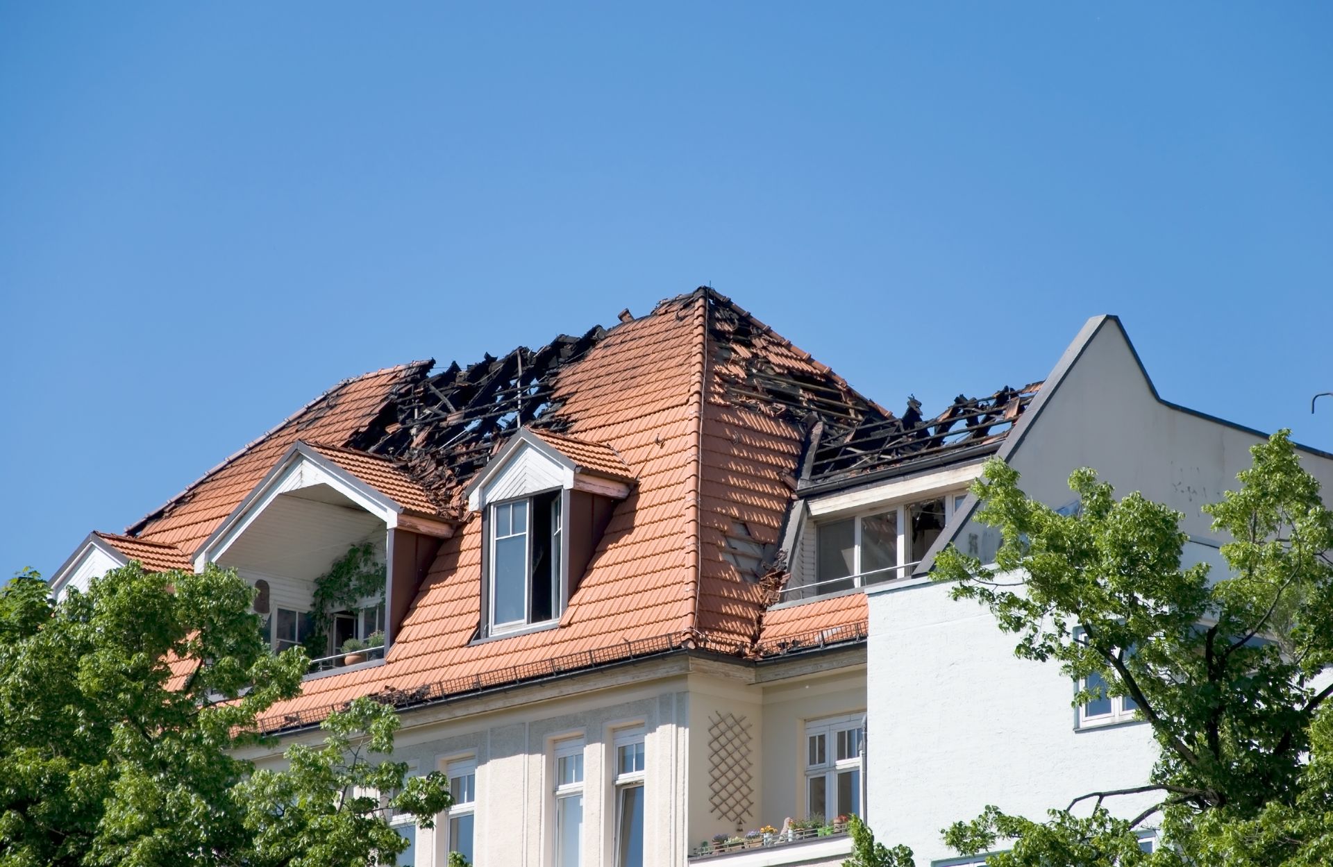 Roof of a building damaged by fire, charred areas visible, red tiles, clear blue sky.