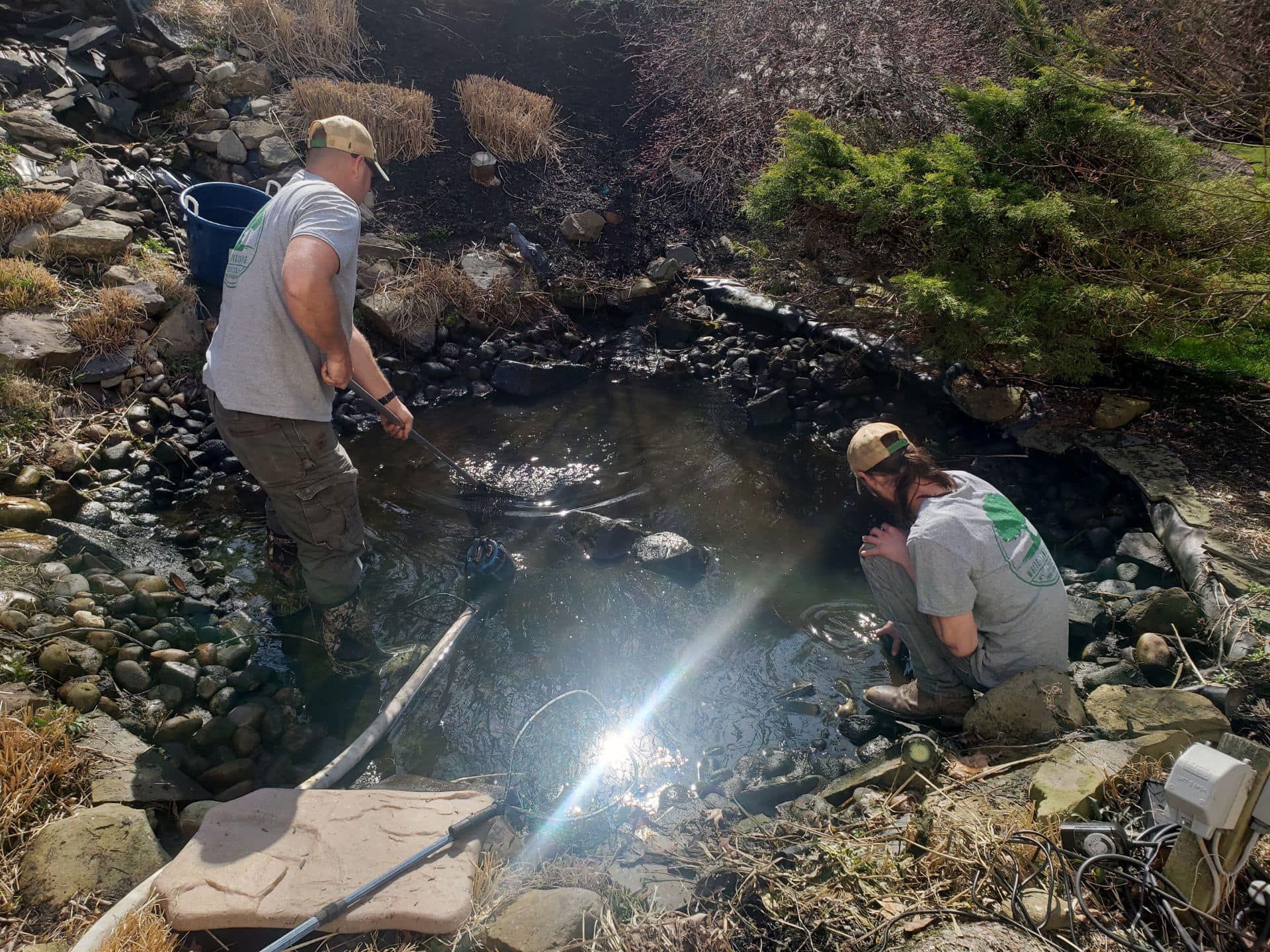 Two men are cleaning a stream with a hose