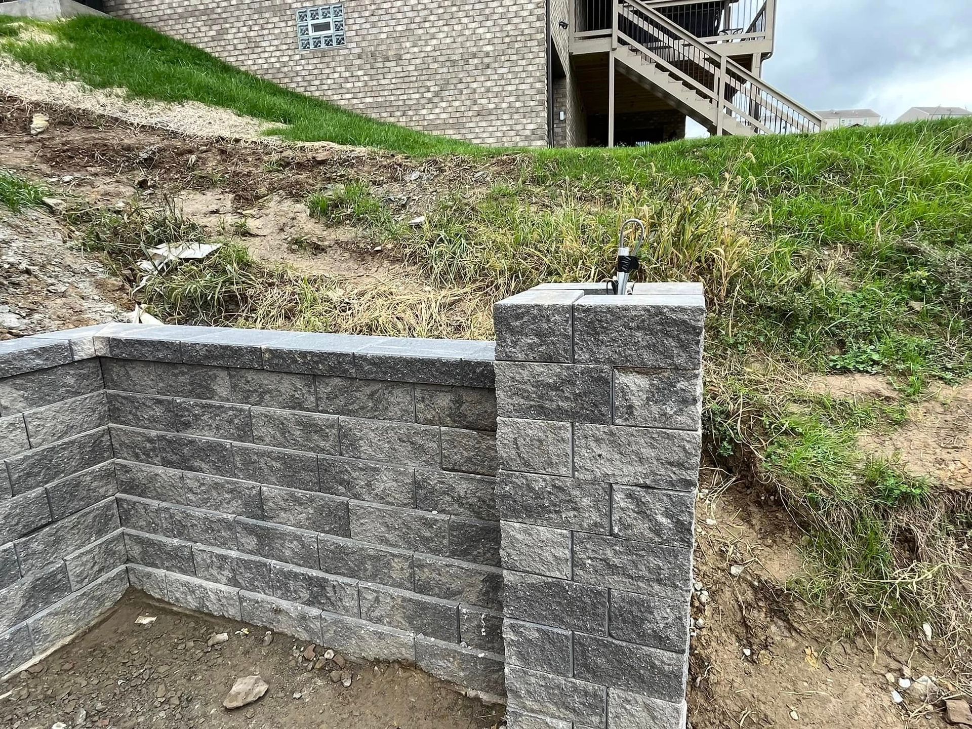 A brick wall is being built in front of a house on a hill.