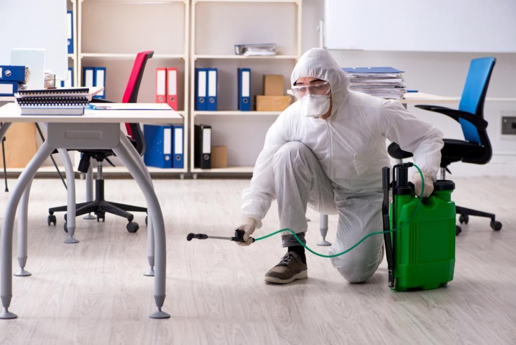 A man in a protective suit is disinfecting an office.