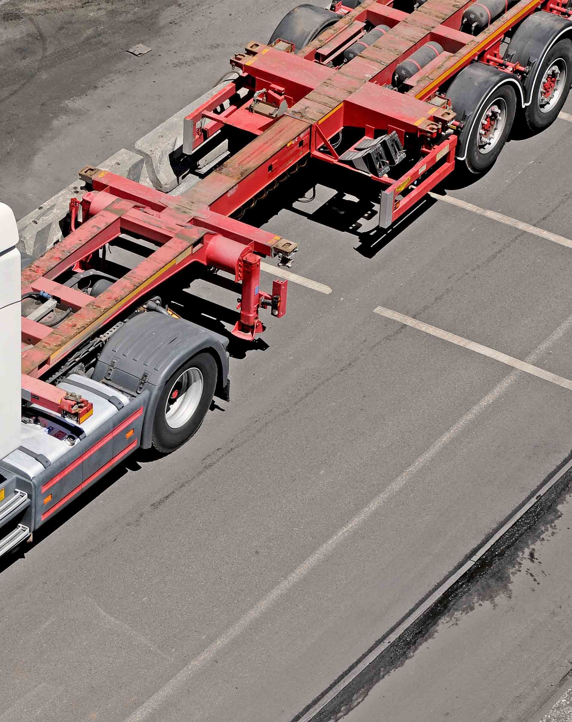 Red and silver truck hauling an empty container chassis on asphalt parking lot. Red and silver truck hauling an empty container chassis on asphalt parking lot.