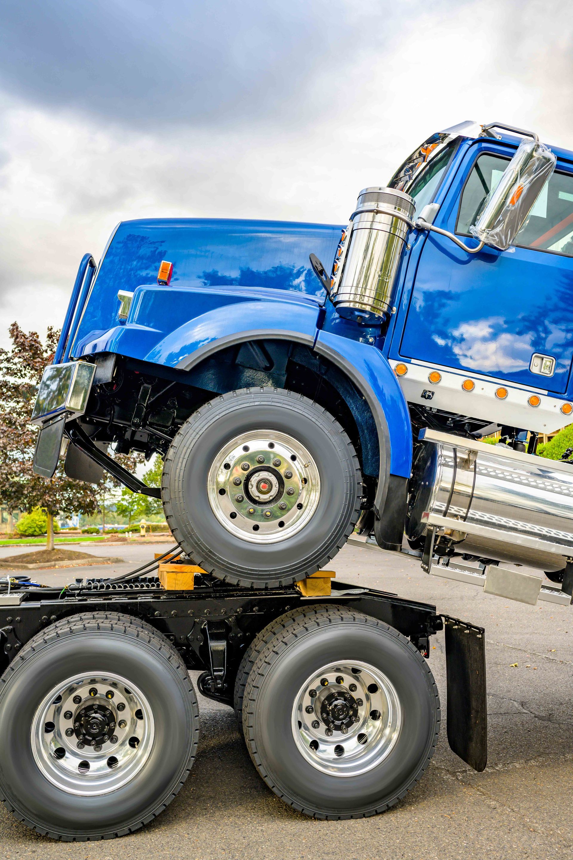 Blue semi-truck cab on top of the truck's rear axle. Wheels visible, parked outdoors on asphalt. Blue semi-truck cab on top of the truck's rear axle. Wheels visible, parked outdoors on asphalt.