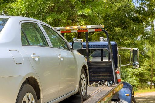 Silver car being towed by a blue tow truck on a sunny day.