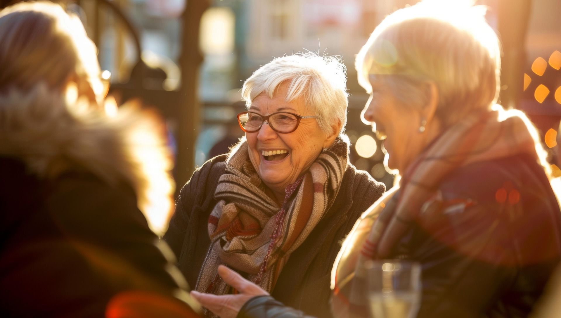Smiling people chatting outdoors in warm golden sunlight, with blurred lights in the background