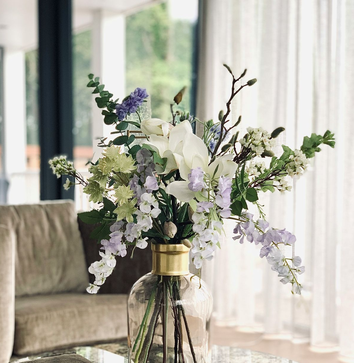 White and lavender flowers in a glass vase on a table in a bright living room