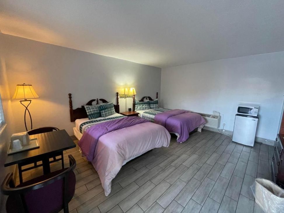A hotel room with two beds , a table , chairs and a microwave.