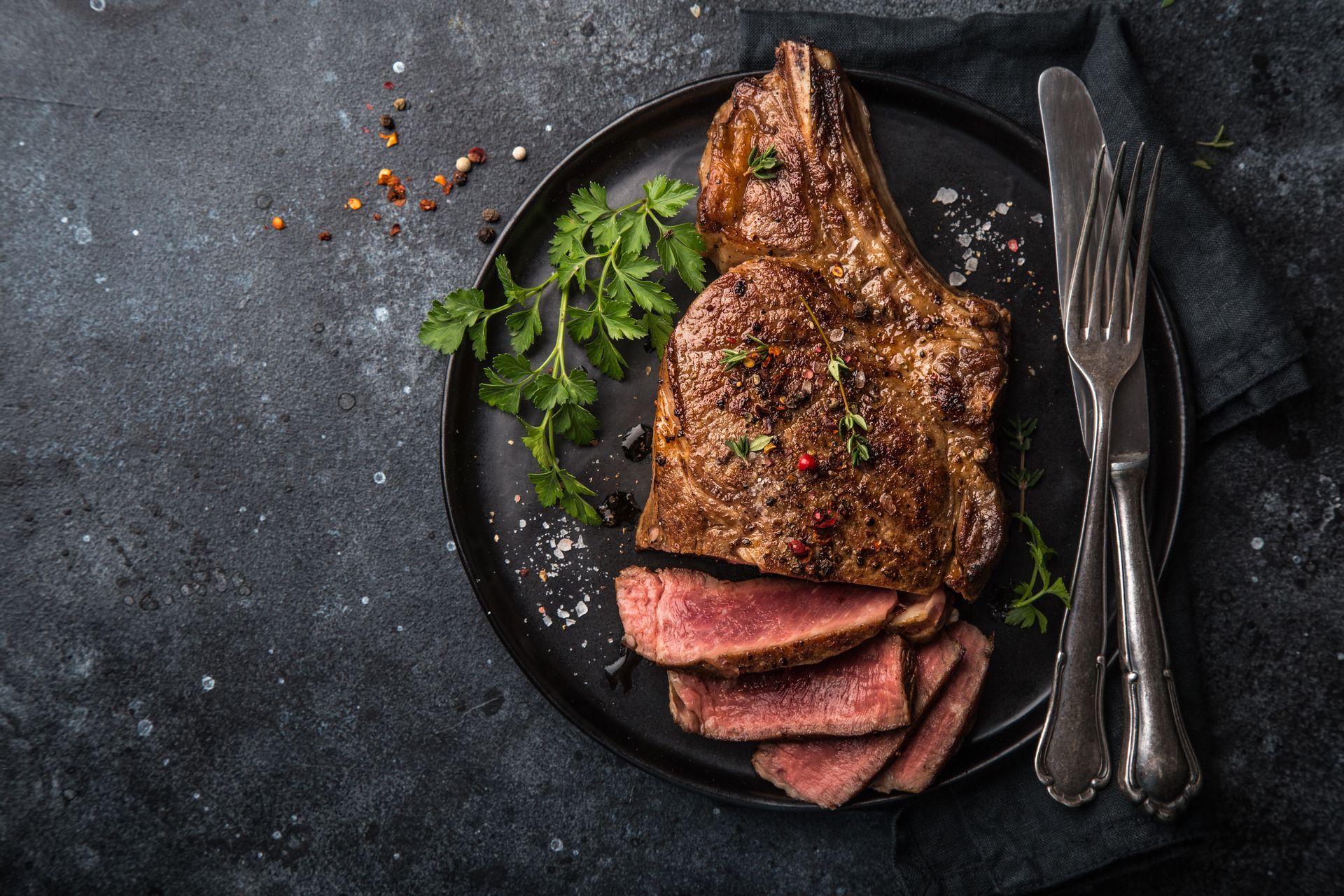 Steak on a plate with vegetables and utensils.