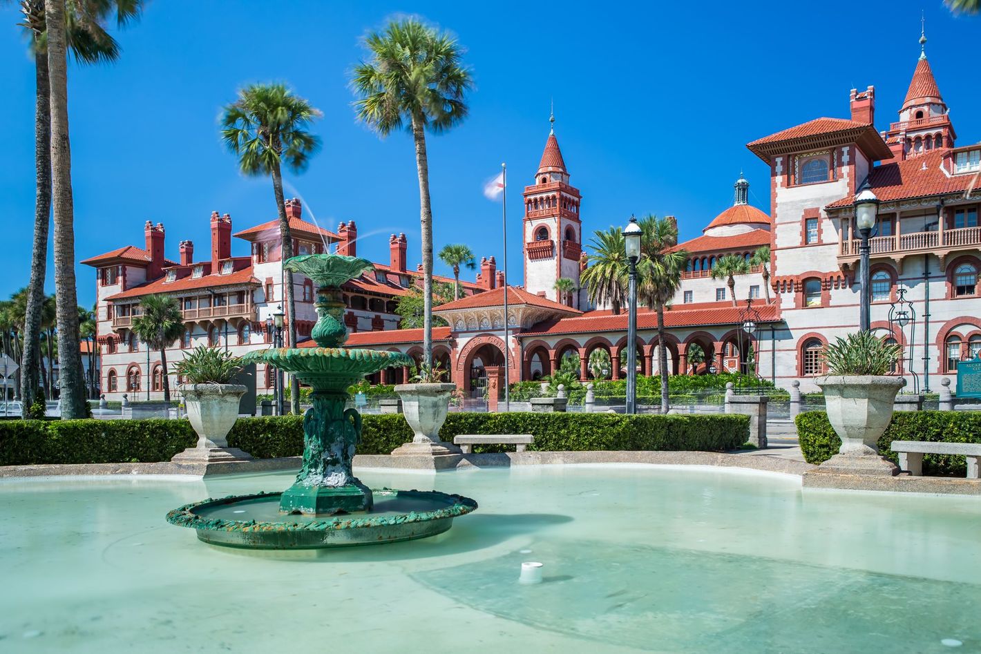 A fountain in front of a large building with palm trees in front of it.
