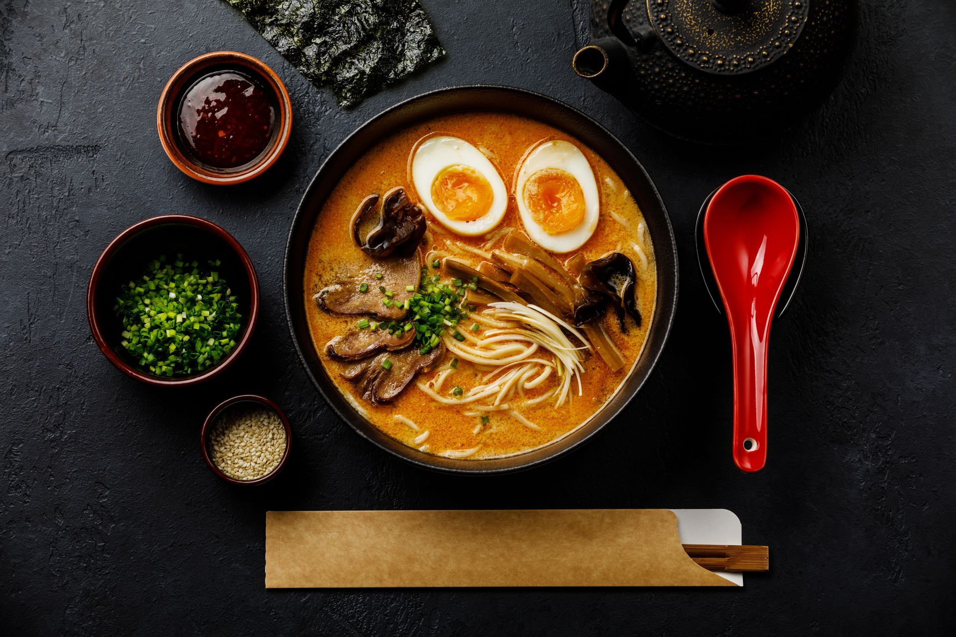 A bowl of ramen with eggs and chopsticks on a table.
