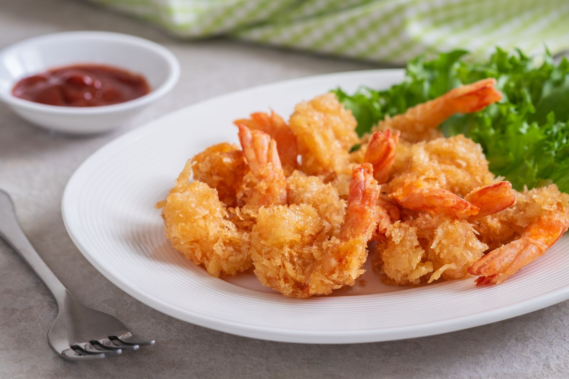 A plate of fried shrimp with lettuce and ketchup on a table.