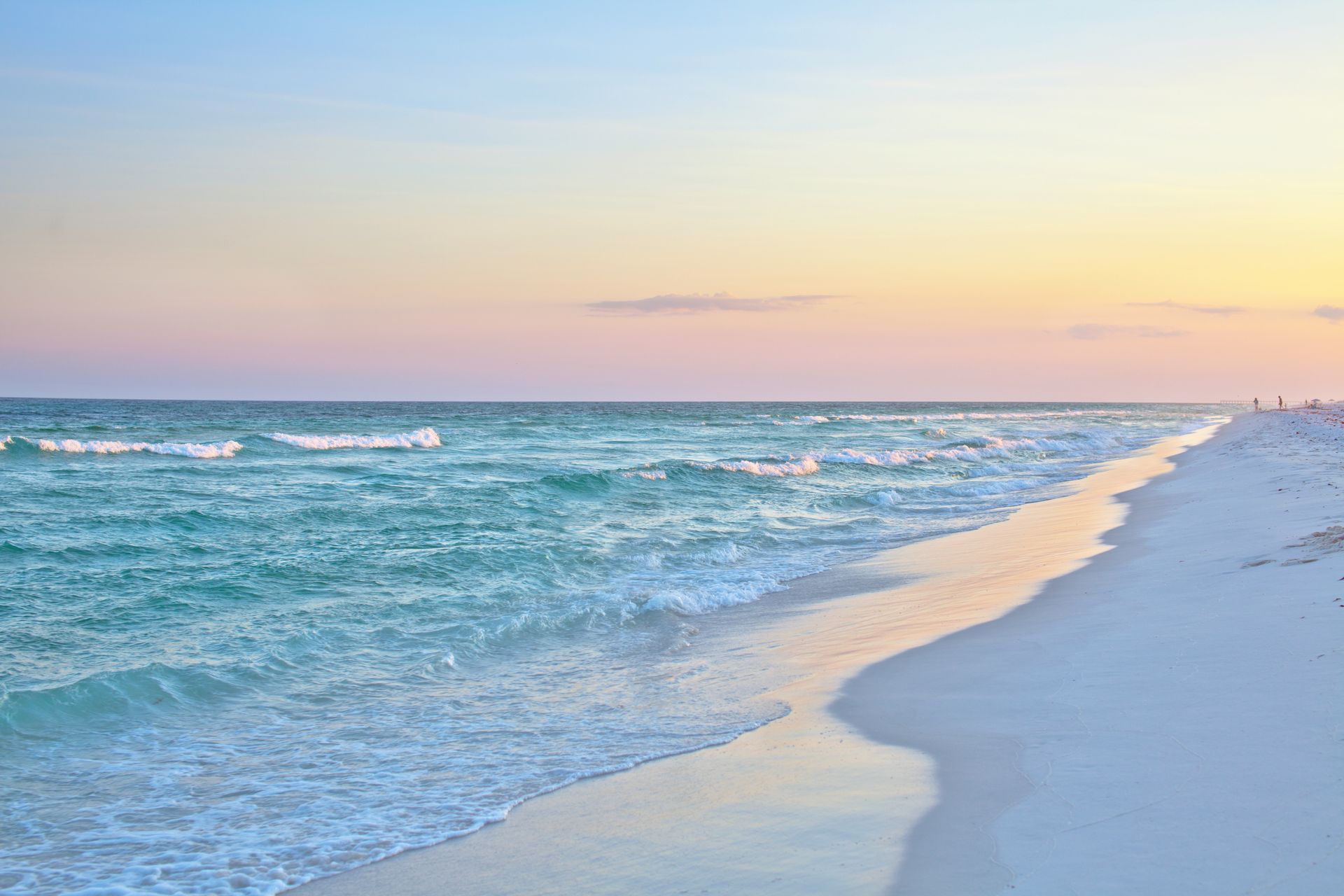 A sandy beach with waves crashing against the shore at sunset.