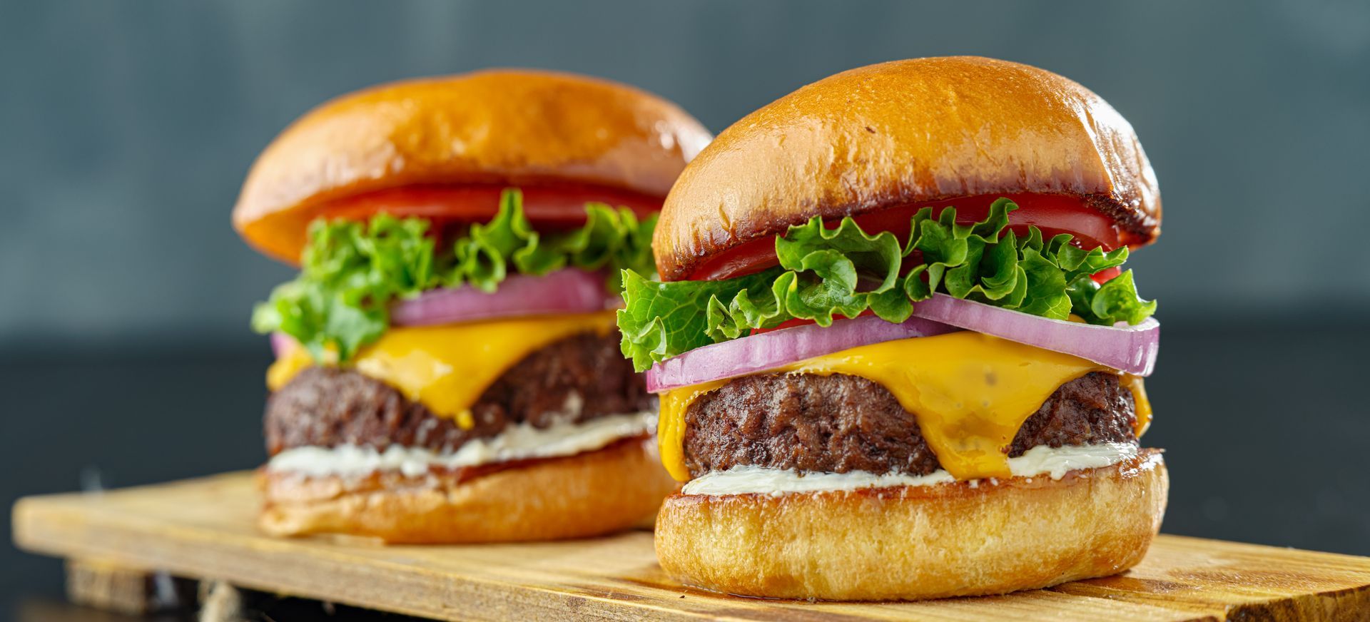 Two hamburgers are sitting on a wooden cutting board.