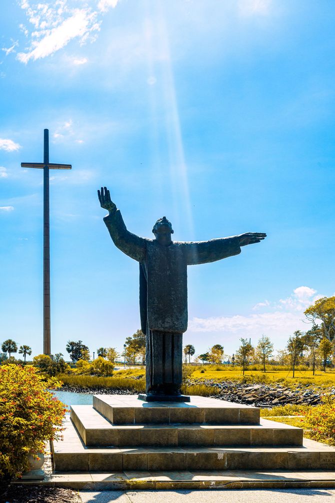 A statue of jesus with his arms outstretched and a cross in the background.