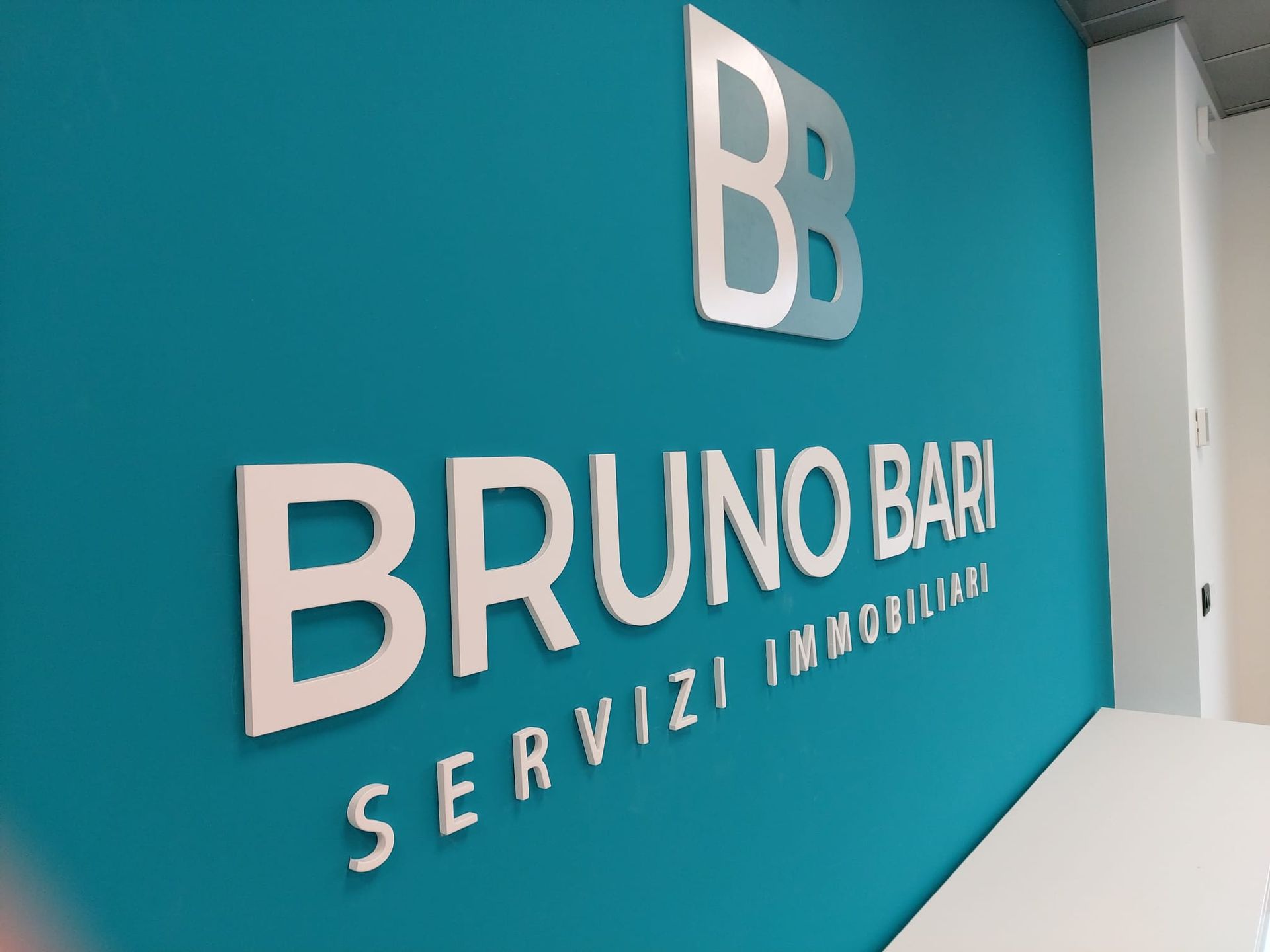 Insegna murale blu con la scritta “BRUNO BARI SERVIZI IMMOBILIARI” e logo BB bianco.