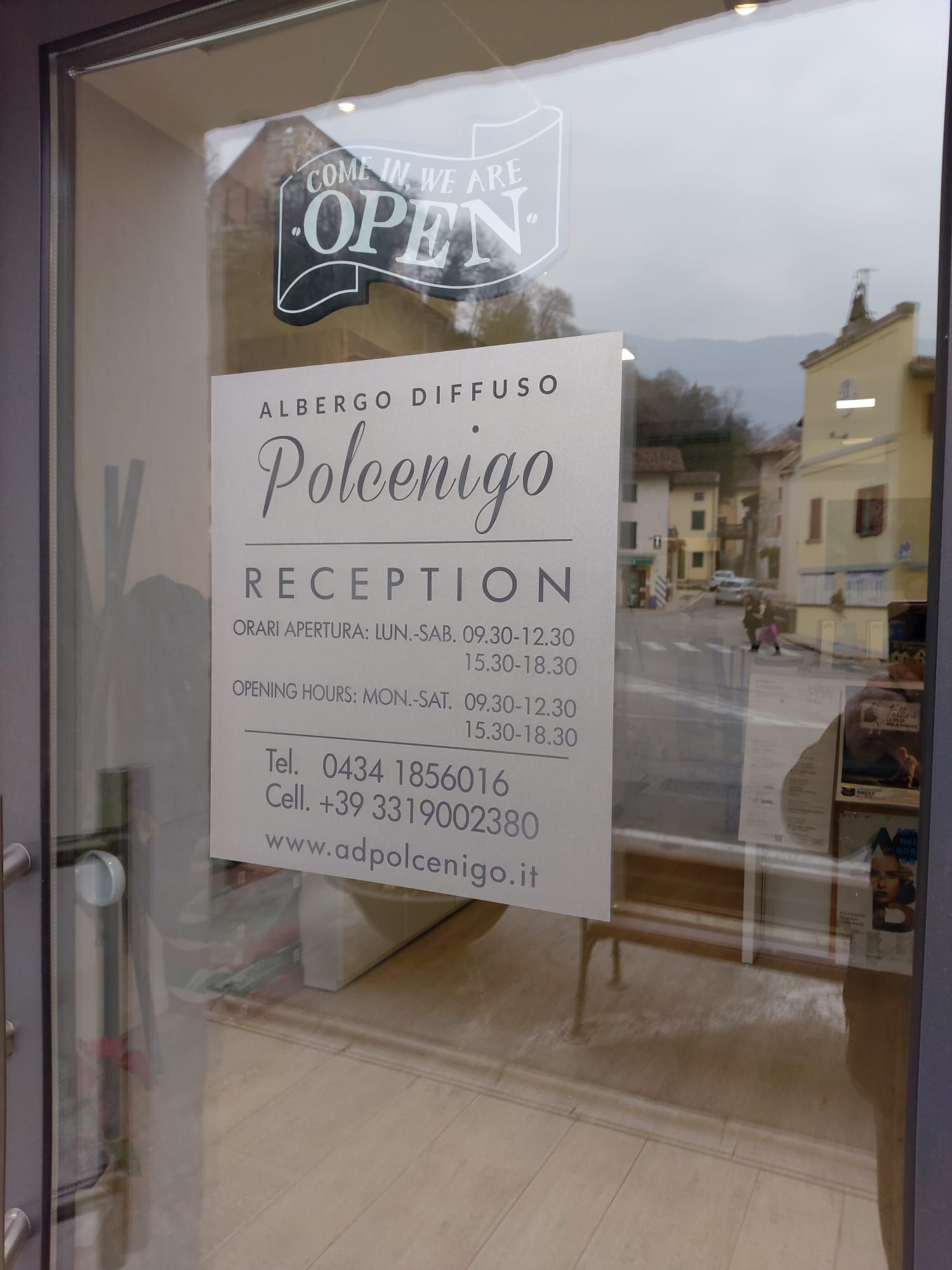 Insegna della reception dell'Albergo Diffuso Polcenigo su una porta a vetri, con orari di apertura e recapiti.