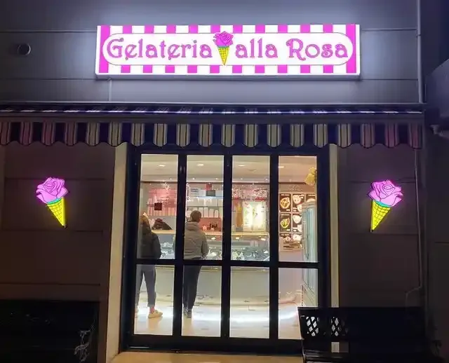 Vetrina illuminata di notte di una gelateria con insegna rosa recante la scritta 