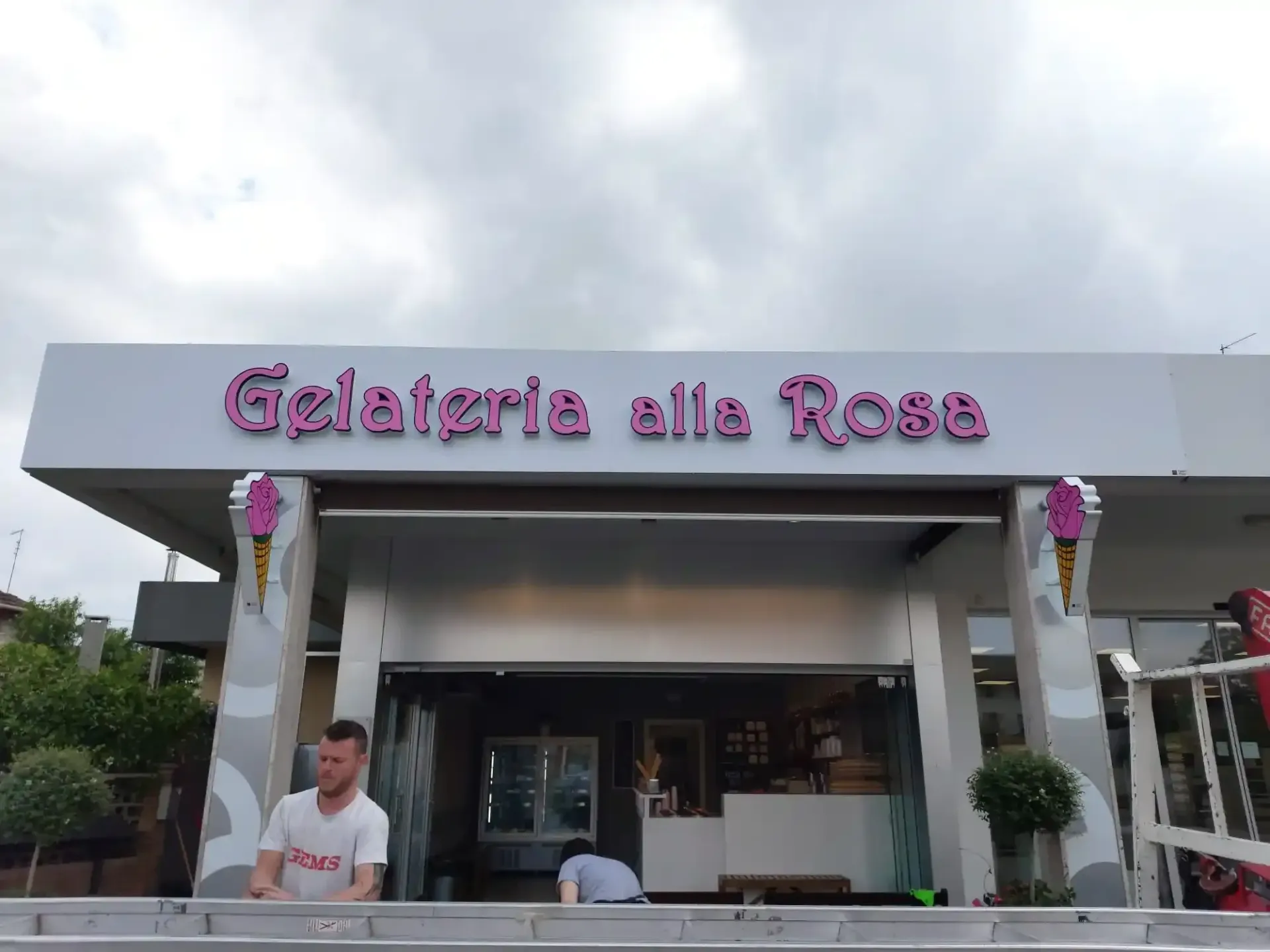 La gelateria alla Rosa ha una vetrina con insegna rosa e un uomo in piedi all'esterno sotto un cielo nuvoloso.