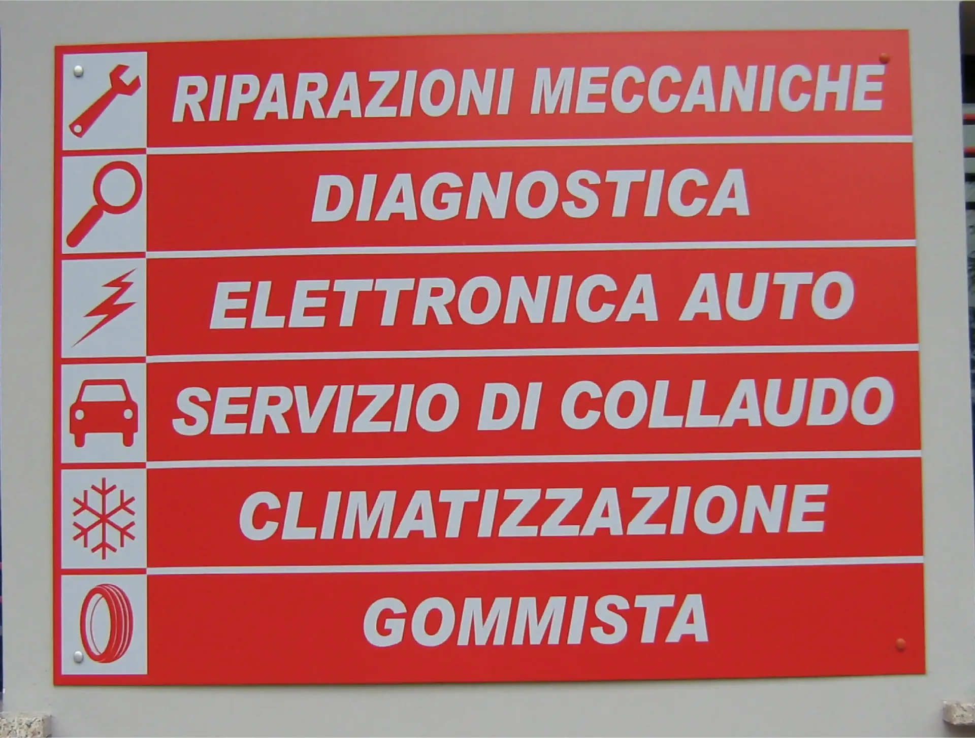 Cartello rosso di officina con servizi auto: riparazioni, diagnostica, elettronica, collaudo, climatizzazione, gommista