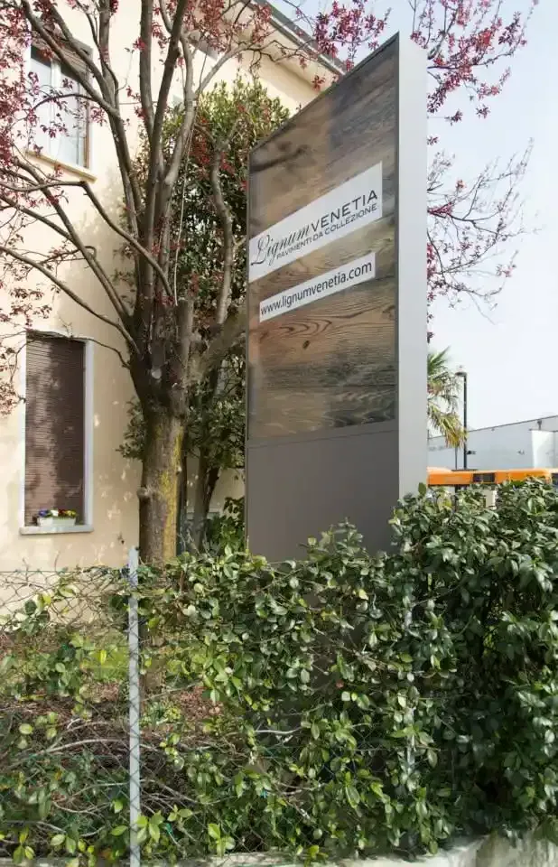 Cartello d'ingresso moderno dell'edificio accanto a cespugli frondosi e un piccolo albero
