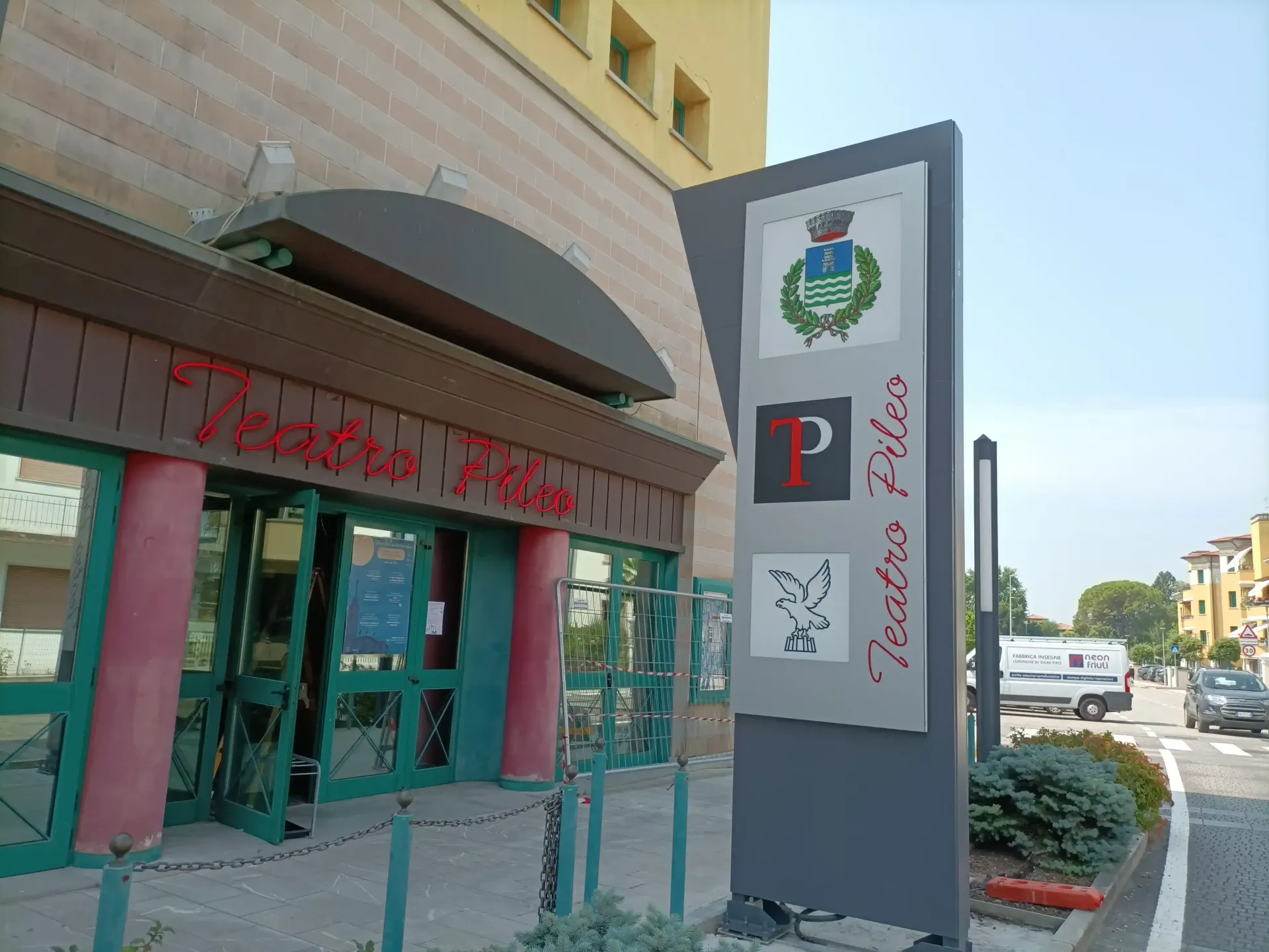 Ingresso del negozio con scritte rosse, porte a vetri e un'alta insegna grigia sul marciapiede.