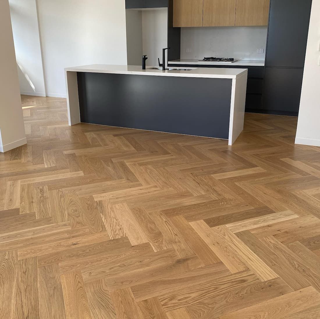 Herringbone hardwood floor in a kitchen with a gray island and light wood cabinets.