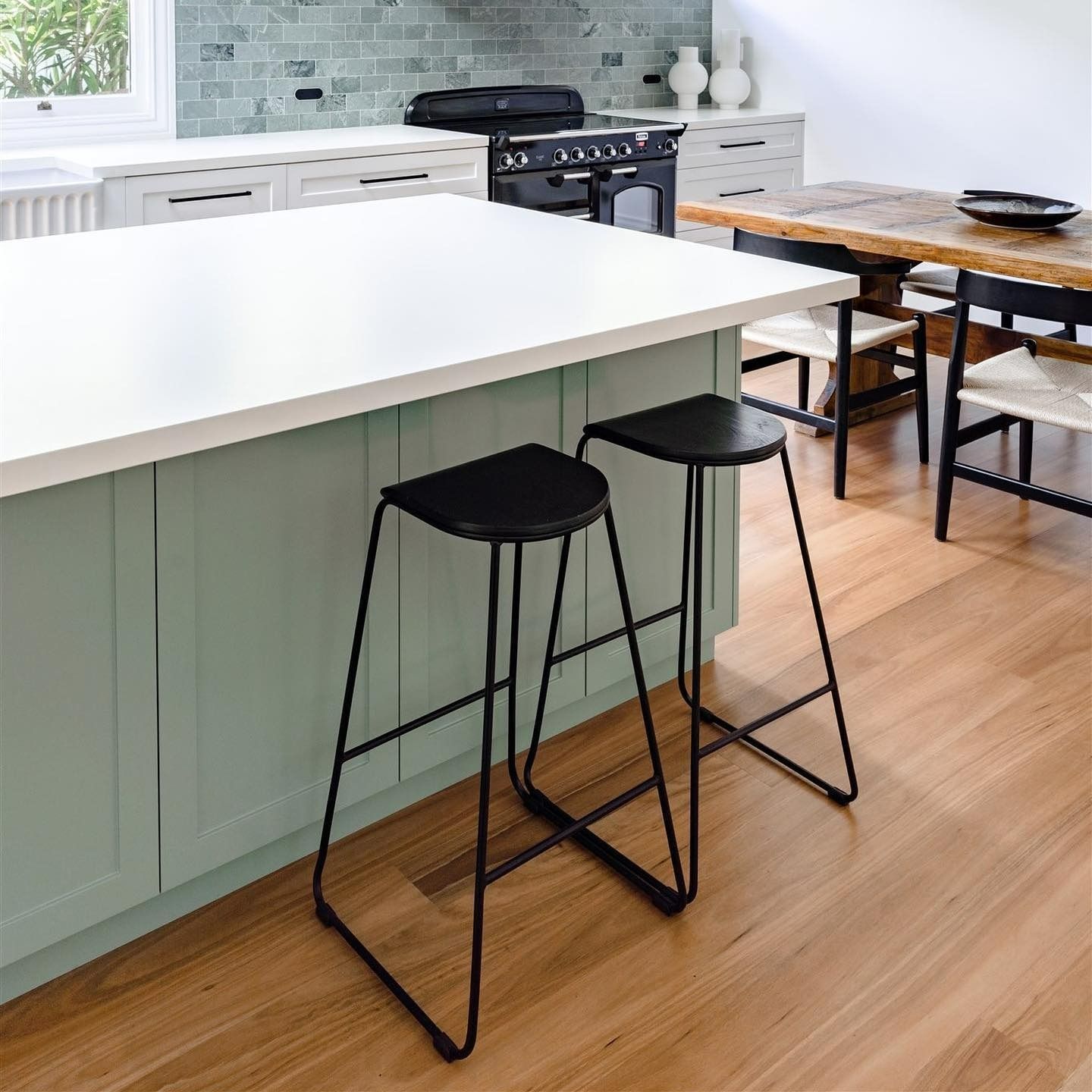 Two black bar stools sit at a light green kitchen island with a white countertop.