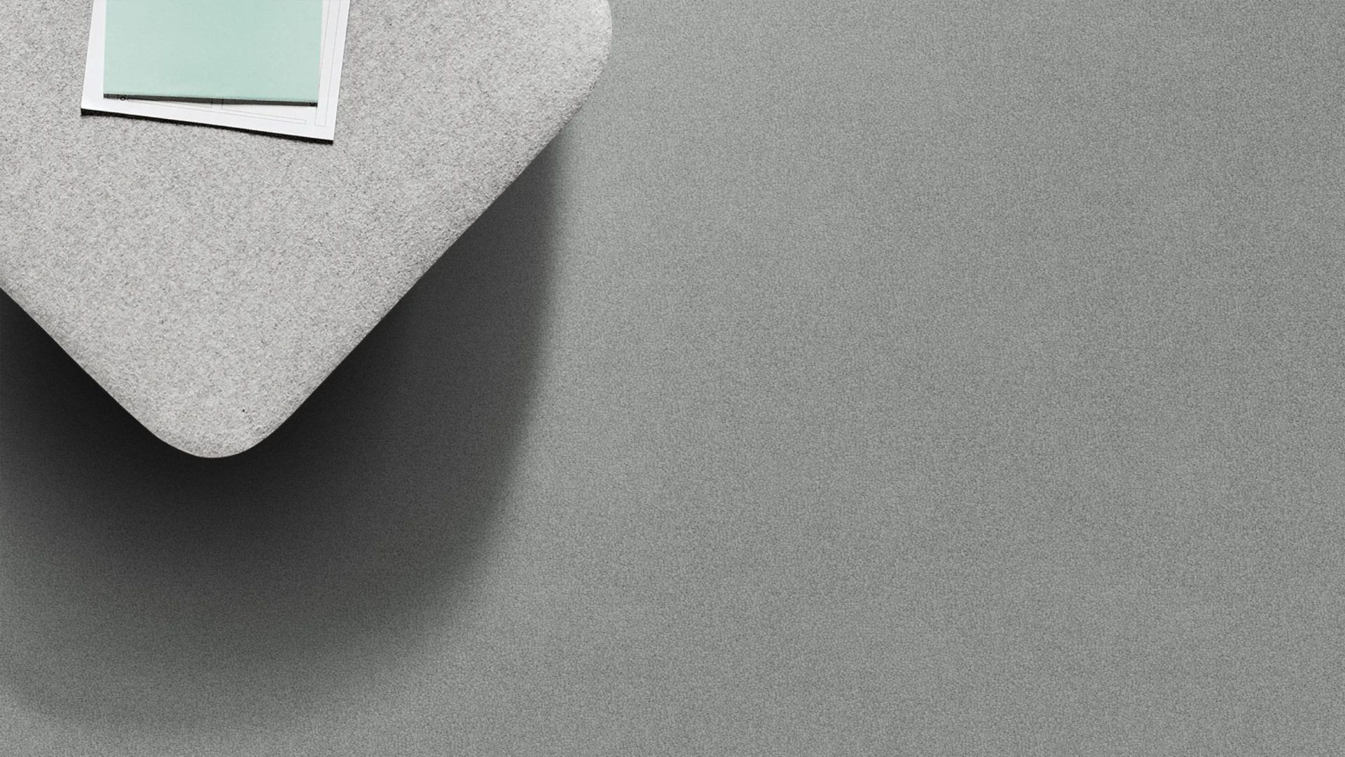Gray, textured surface with a light gray, angular shape in the top left corner; two small papers are on the angular shape.
