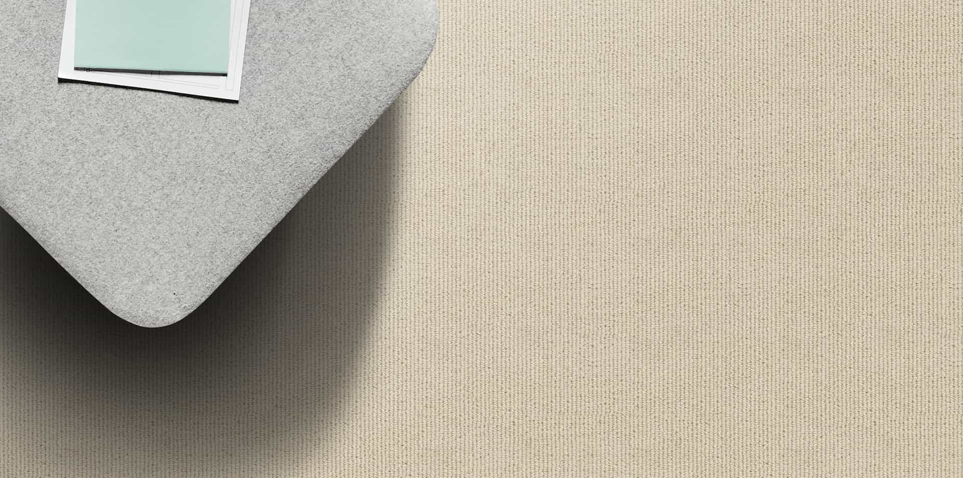 A corner of a gray fabric object partially covers a beige textured surface. Light blue and white squares are placed on top.