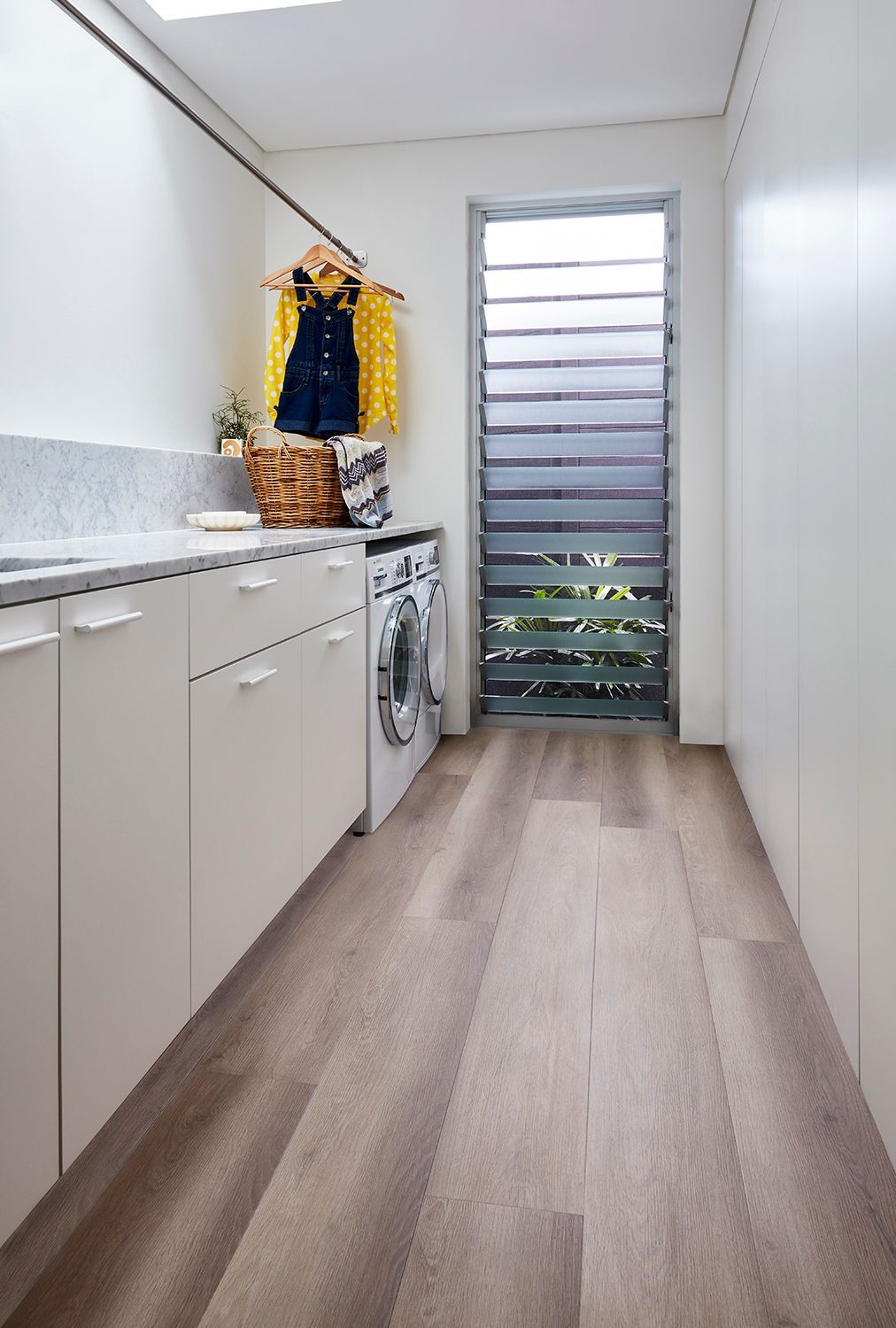 Laundry room with white cabinets, washing machine, wooden floor, and a slatted window.