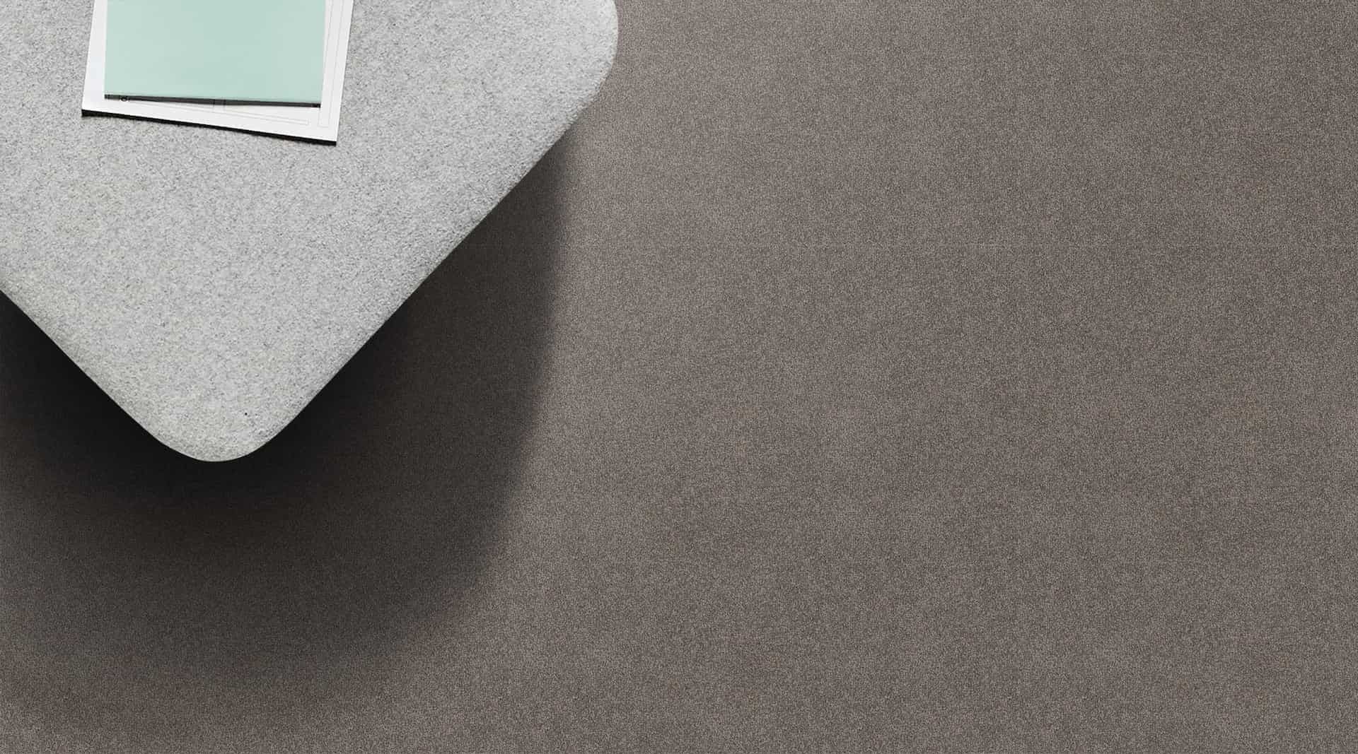 A gray, heart-shaped object on a textured surface, with a small teal and white square on top left.