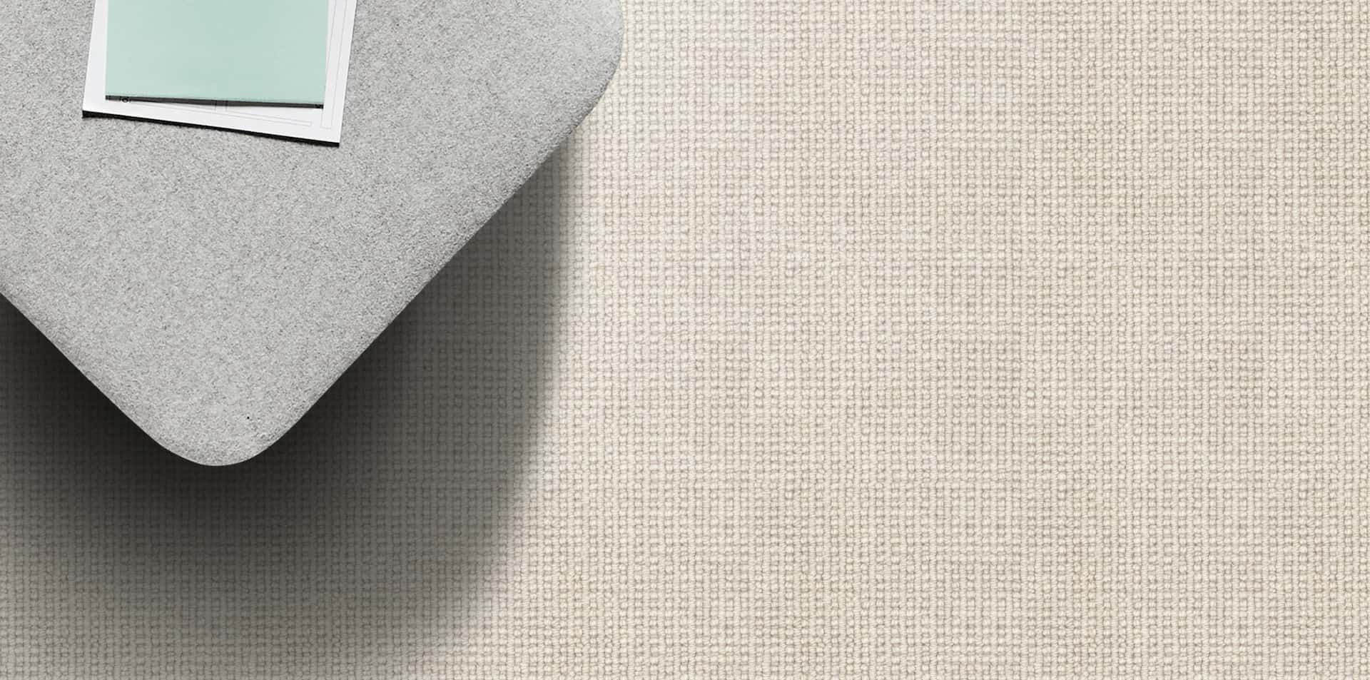 A corner of a light gray fabric surface with a light textured background. Two small items are on the surface.