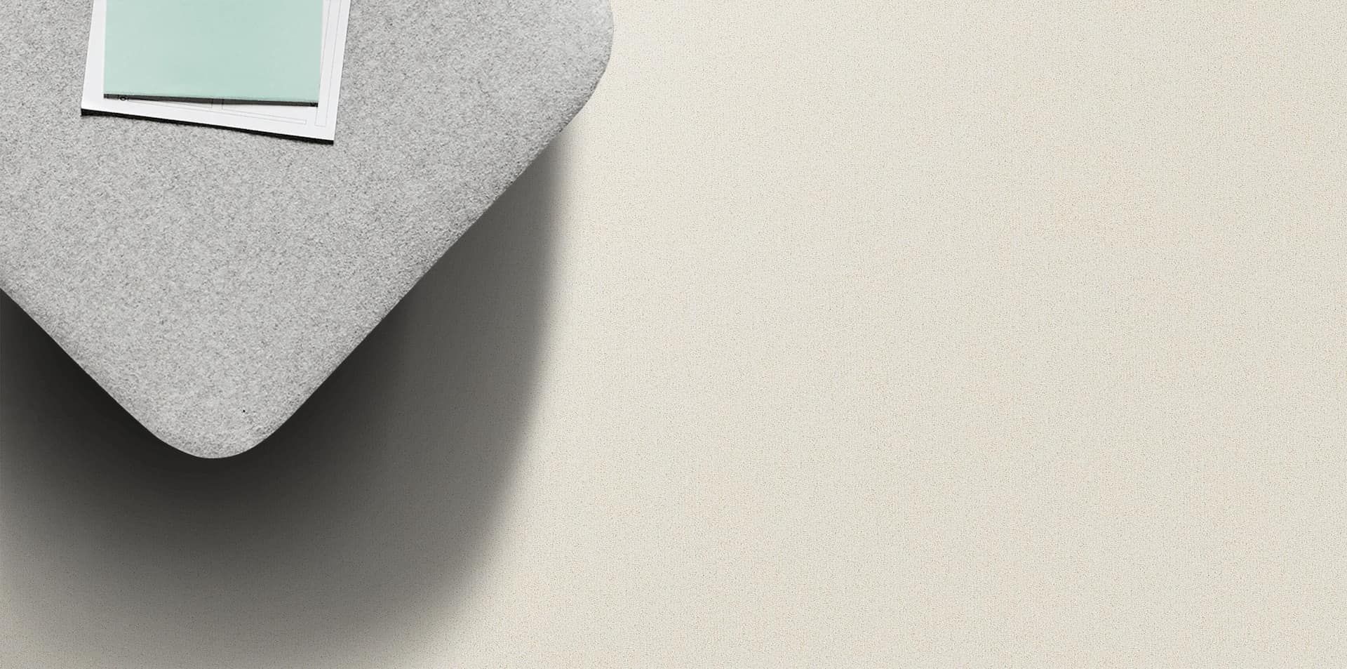 A gray corner of a rug with a light-colored surface; a square of blue and white paper is on top.