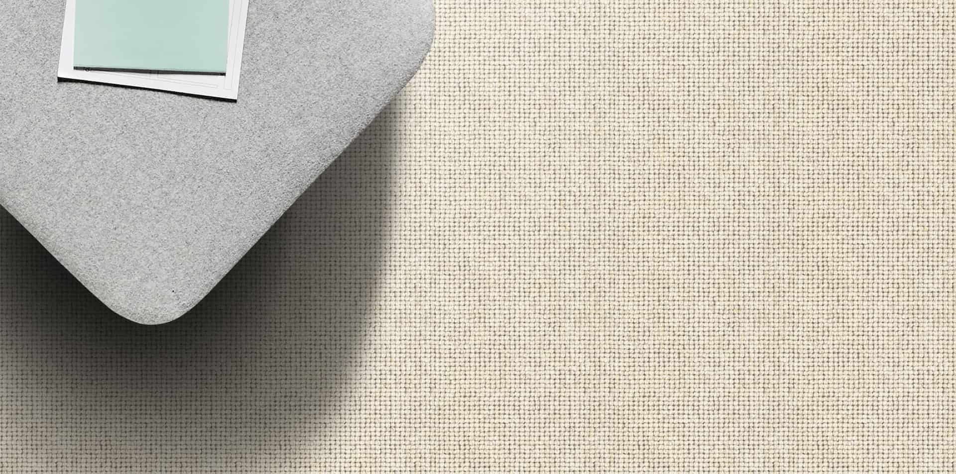 A gray, heart-shaped pillow rests on a woven tan rug. A rectangular object sits on the pillow.