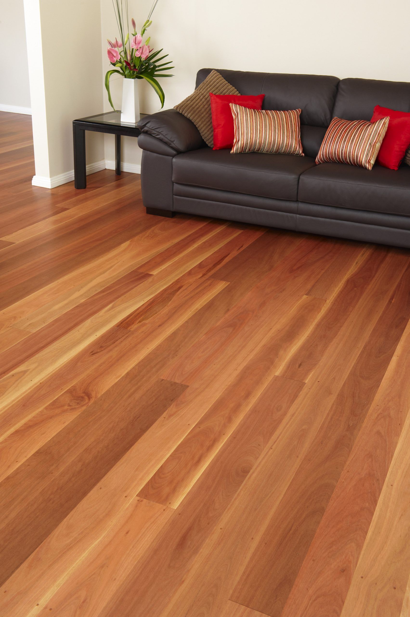 Hardwood floor in a living room with a dark brown leather couch, cushions, and a table with flowers.