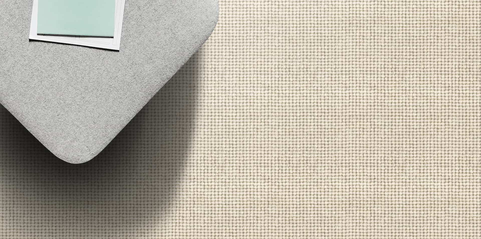 A gray textile with a small corner flipped up, a blank card is on it. The surface is textured in a neutral color.