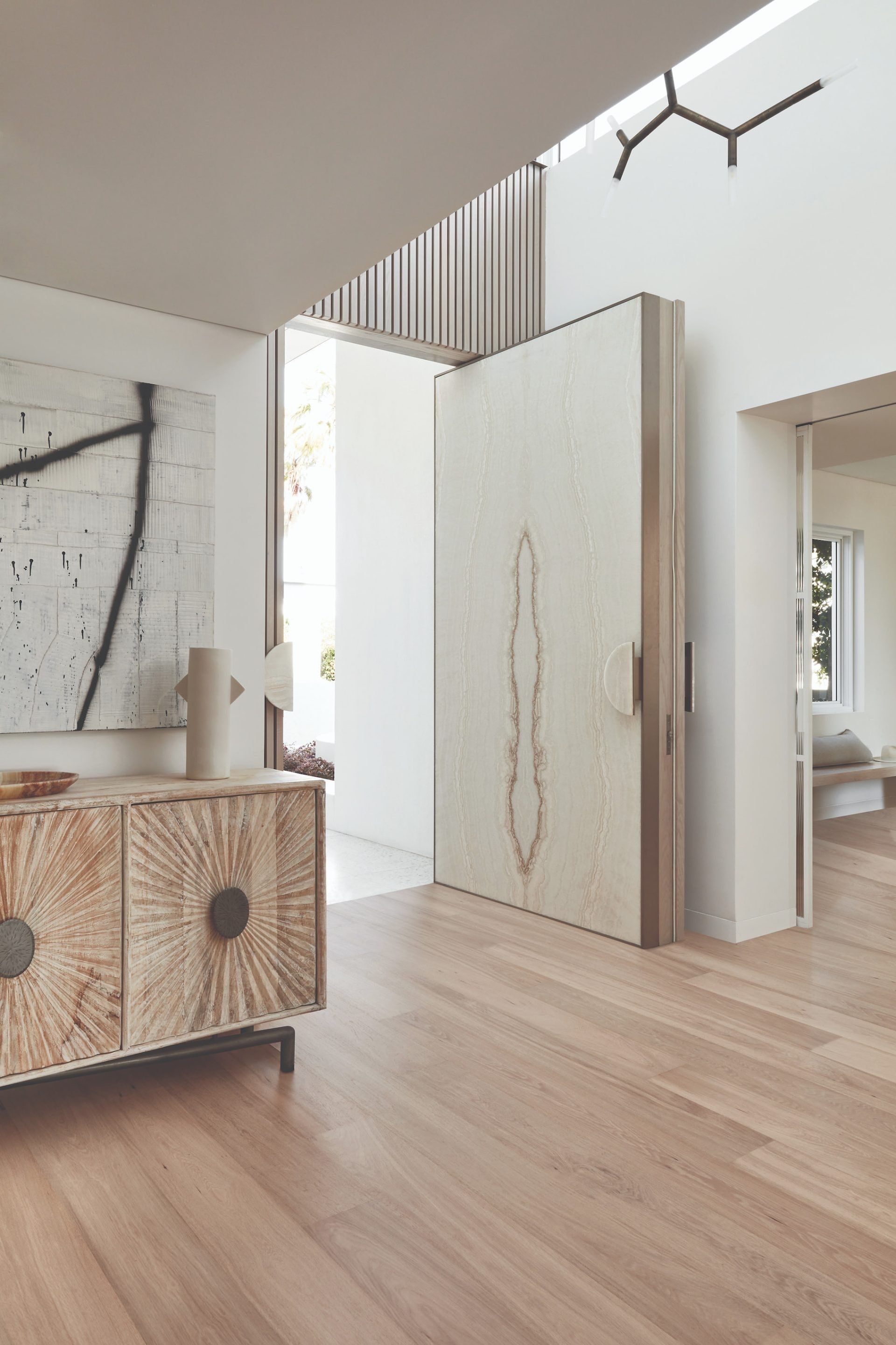 Light wood-floored entryway with open doorway, large art piece, and a wood sideboard.